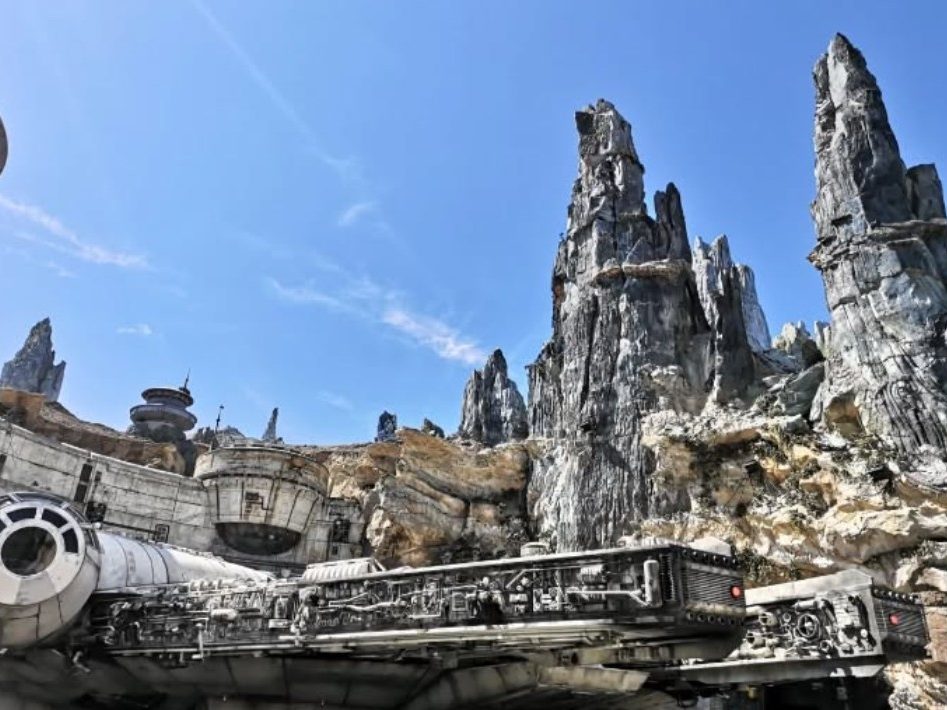 Rocky formations rise against a clear blue sky, with a detailed spaceship in the foreground.