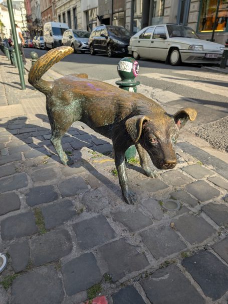A bronze sculpture of a dog weeing on a cobbled street in Brussels. Known as Zinneke Pis.