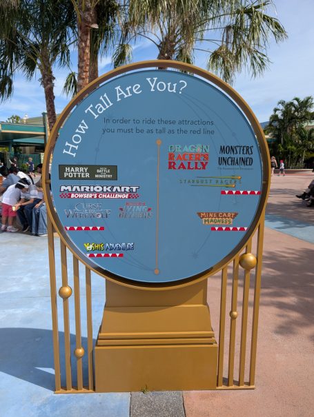 Height measurement sign with various height restrictions for rides and attractions.