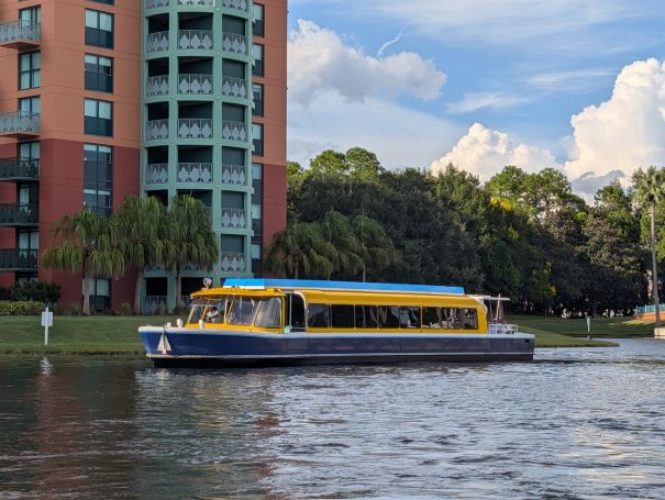 A blue and yellow boat glides along a river near a tall residential building.