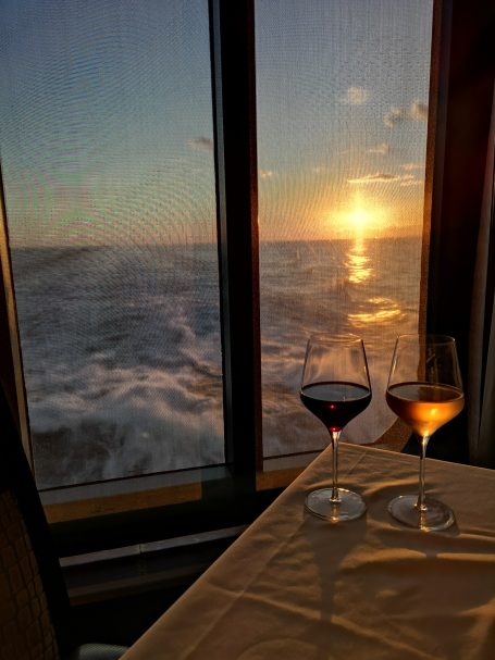 Two glasses of wine on a table with a view of a sunset over the ocean.