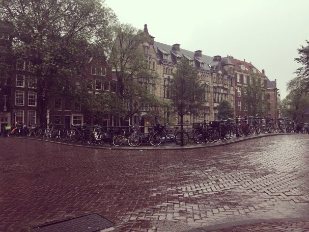 Rainy street scene in Amsterdam with historic buildings and parked bicycles.