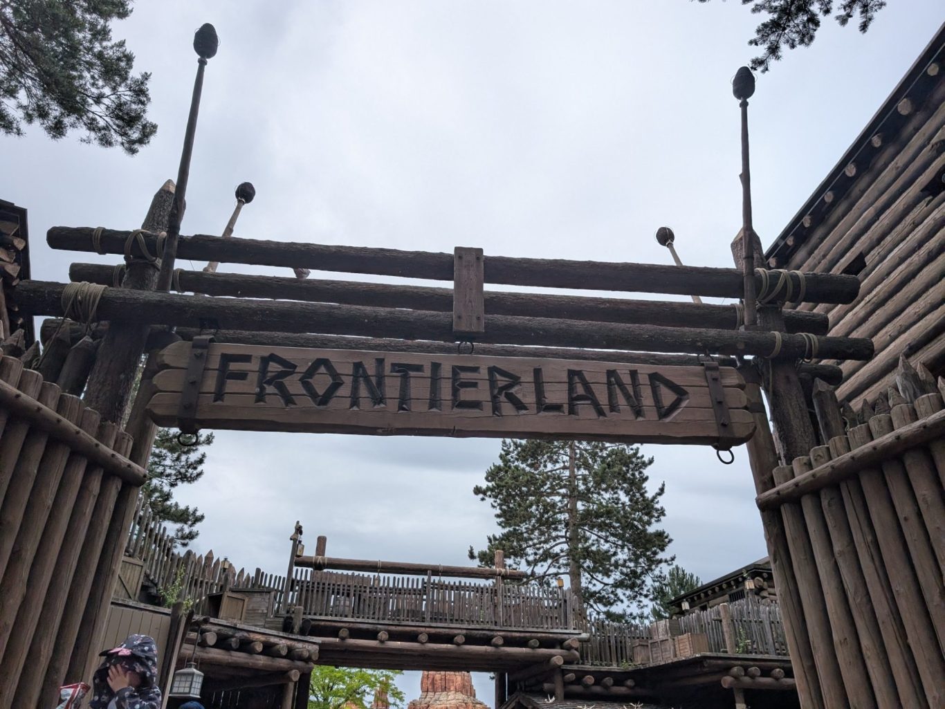 Entrance sign to Frontierland with wooden beams and a cloudy sky.