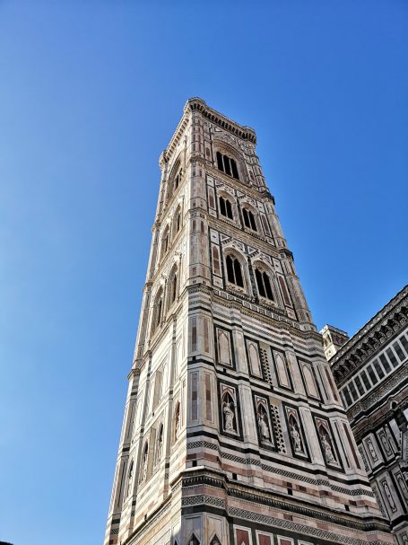 The Giotto's Campanile, a tall medieval bell tower with intricate stone facades against a blue sky.
