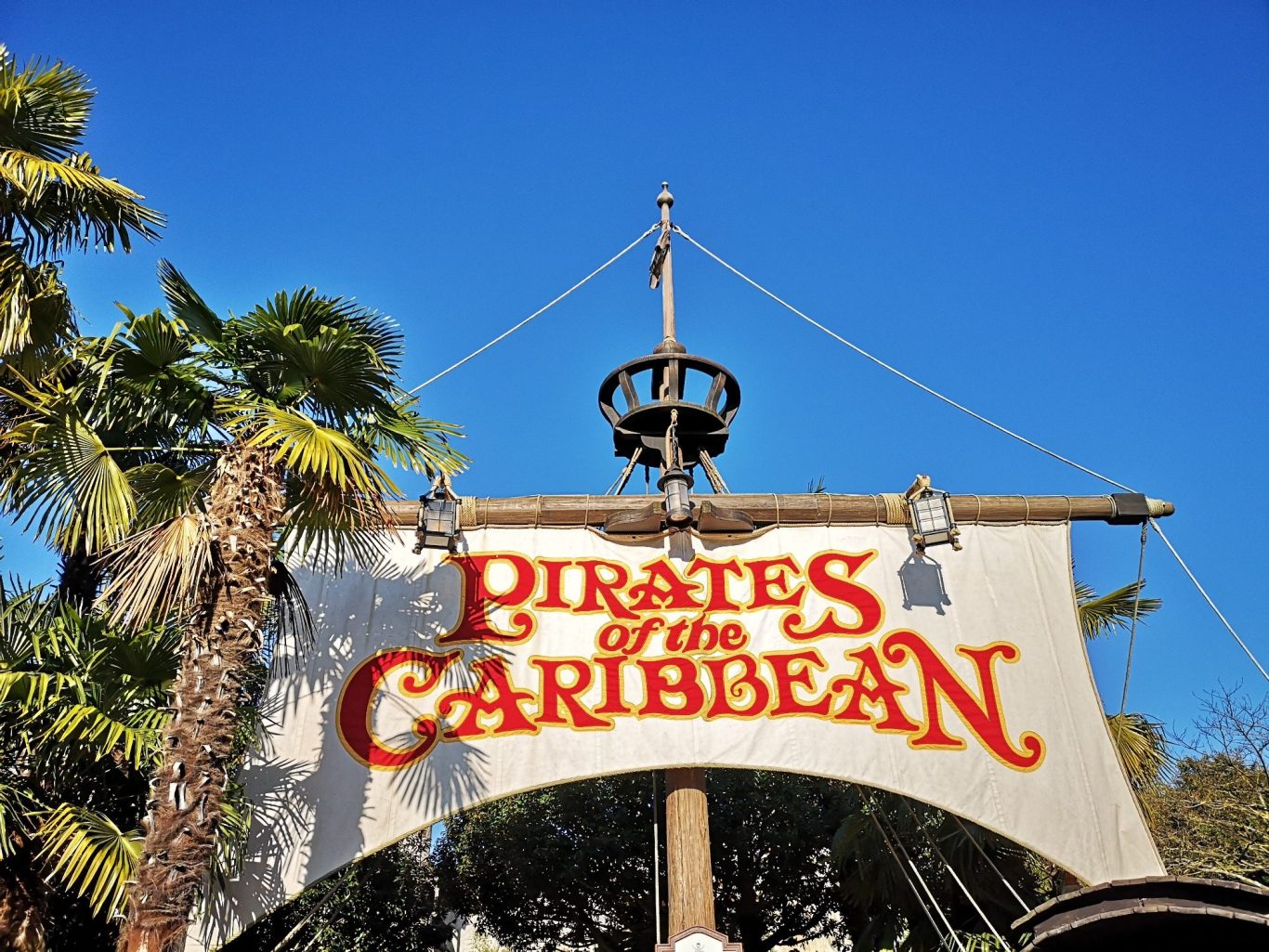 Sign for "Pirates of the Caribbean" with palm trees and blue sky in the background.