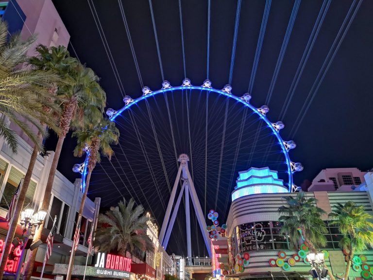 The illuminated High Roller at night, surrounded by palm trees and city buildings, located in Las Vegas.