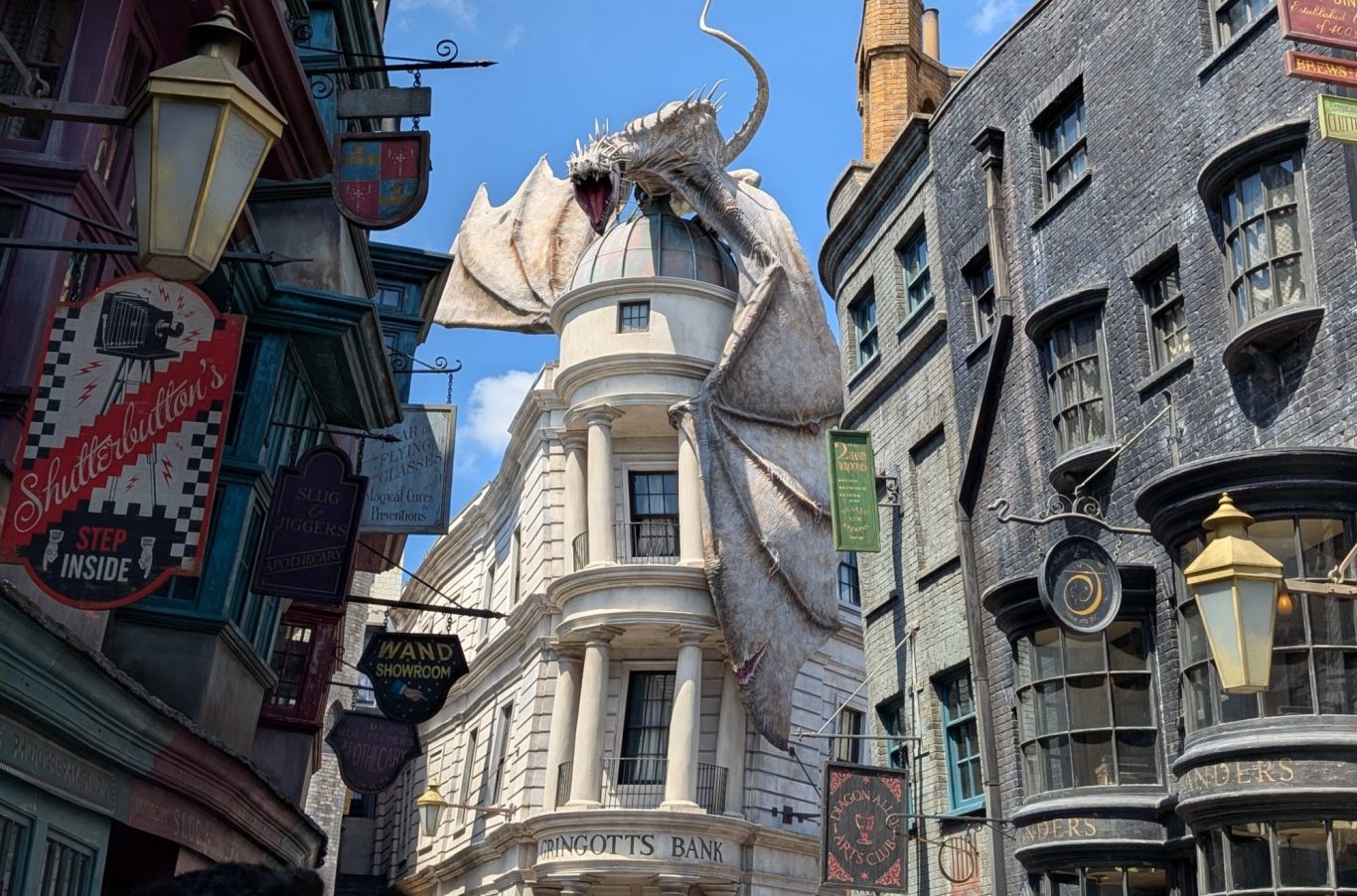 A white, dragon-like creature atop a whimsical building in a cobbled street setting.