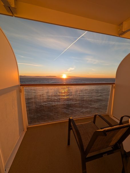 Sunset over the ocean viewed from a balcony with a chair in the foreground.