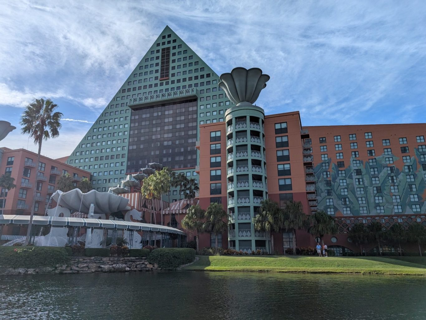 The exterior of a distinctive hotel with a triangular glass structure and palm trees.