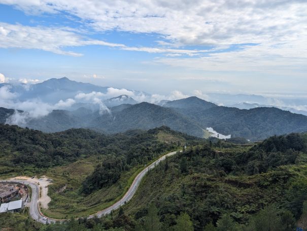Scenic view of Genting Highlands, a view of rolling hills and a winding road under a cloudy sky.