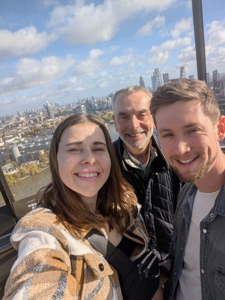 I&B's Founder, Husband and Dad posing in The Chimney Lift with the London skyline under a cloudy sky in the background.