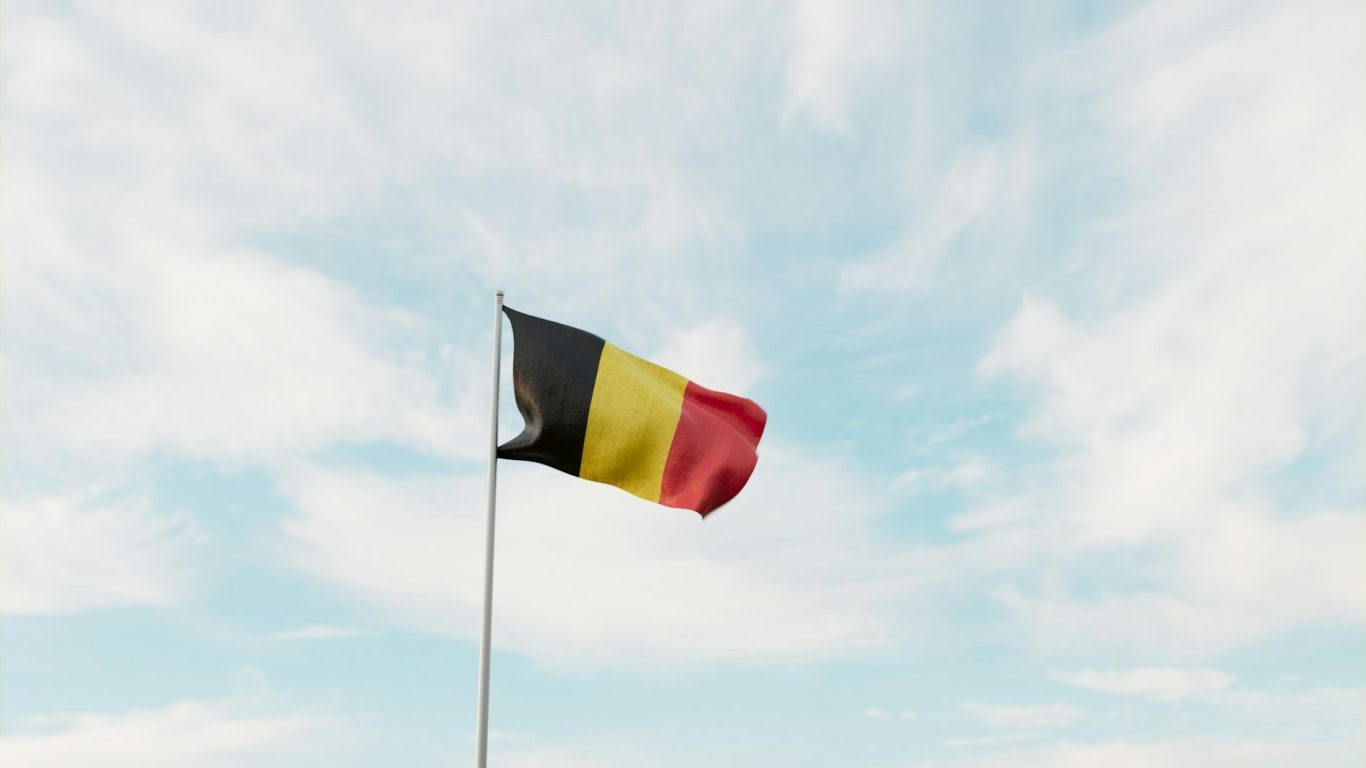 Belgian flag fluttering against a blue sky with scattered clouds.