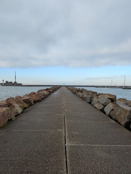 A stone pier stretches out to the water under a cloudy sky.