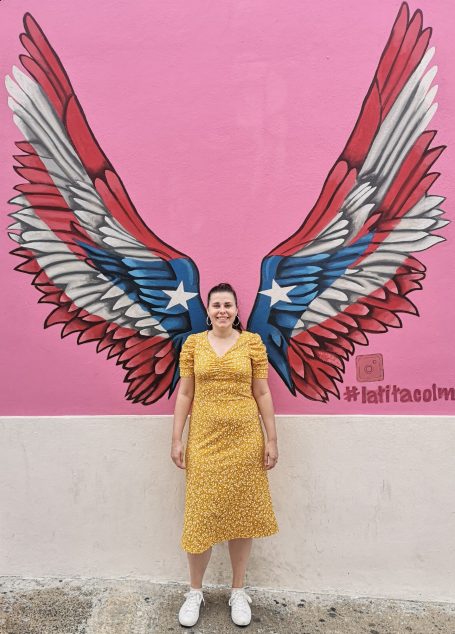 I&B's Founder posing in front of street art wings, in the colours of the Puerto Rico flag.