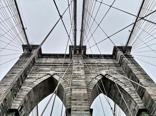 View of the Brooklyn Bridge's arches and overhead cables from below.