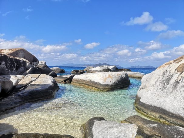 Clear blue water with rocky formations, known as The Baths under a bright sky, surrounded by gentle waves, located at Virgin Gorda.