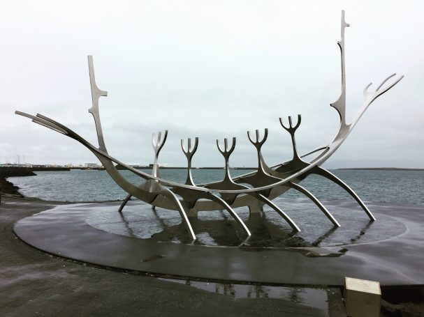 A metal sculpture of a boat with five figures, known as the Sun Voyager, set against a cloudy sea backdrop, located in Reykjavík, Iceland.