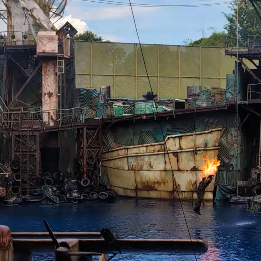 Abandoned ship in a water scene with industrial structures and flames.
