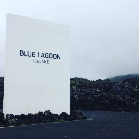 Sign for Blue Lagoon, Iceland, against a rocky landscape and overcast sky.