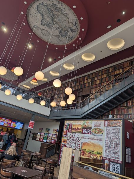 Interior of a modern dining area with hanging lights, a large map on the ceiling, and menu displays.
