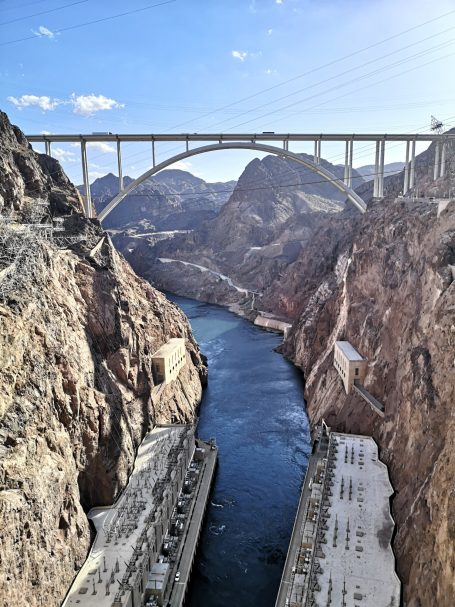 View of the Hoover Dam and bridge over the Colorado River surrounded by rocky cliffs.