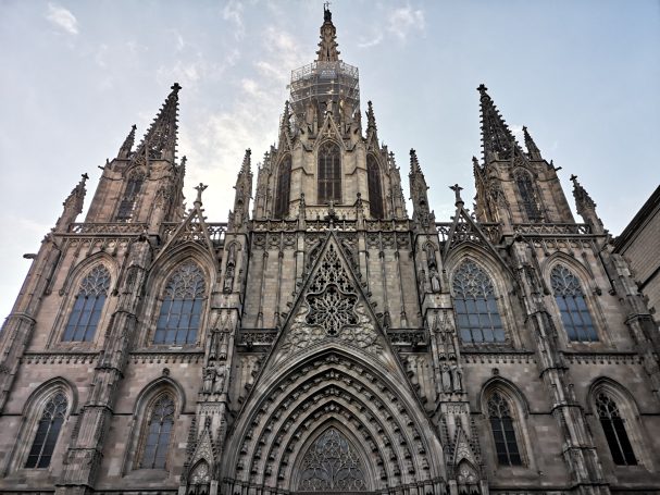 Gothic Barcelona cathedral facade with intricate stonework and tall spires against a clear sky.
