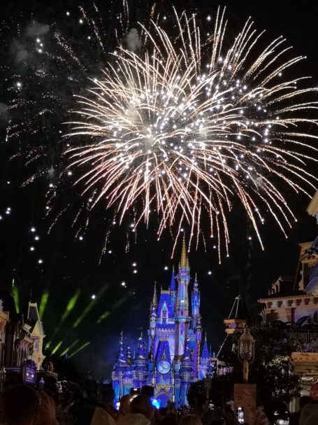 Fireworks illuminate Cinderella Castle at night, with vibrant colours and festive atmosphere.