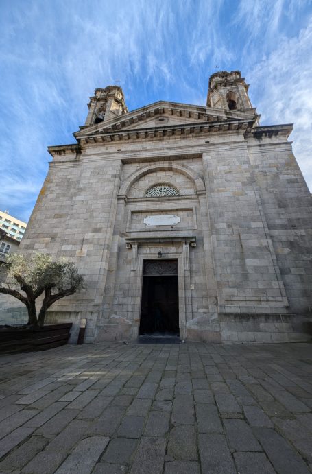 Basílica de Santa María de Vigo, a stone church facade with large entrance and two towers, against a blue sky.