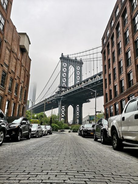 View of the Manhattan Bridge between brick buildings on a cloudy day.