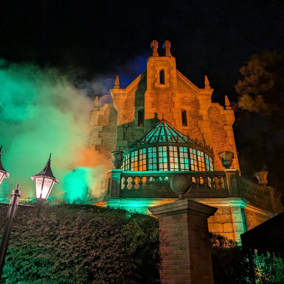Haunted mansion illuminated with green and orange lighting, shrouded in mist.
