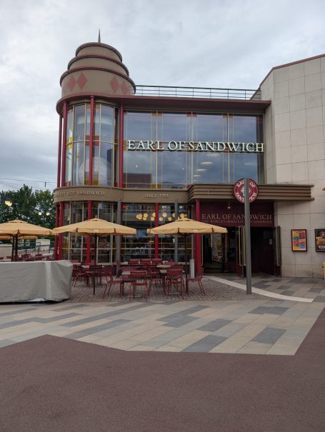 Entrance of a cinema with outdoor seating and umbrellas in a modern setting.