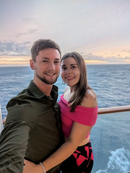 I&B's Founder & Husband posing on a cruise ship balcony with the ocean and sunset in the background.
