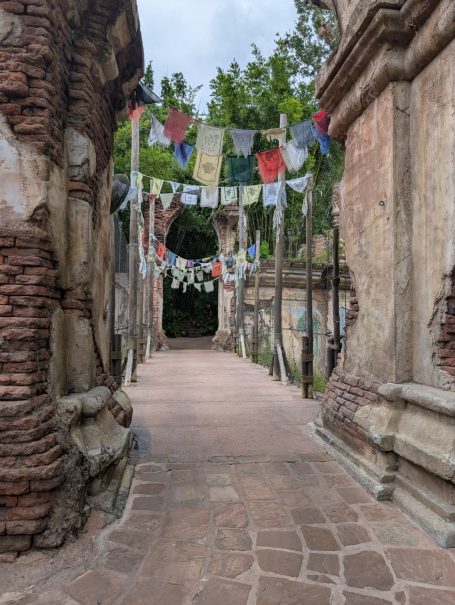 Stone path through ancient ruins, adorned with colourful prayer flags.
