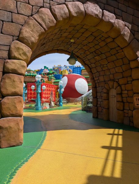 Colourful amusement park scene viewed through a stone archway.