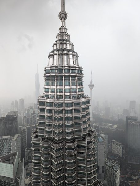 Petronas Towers in a foggy Kuala Lumpur skyline, with the KL Tower and Merdeka 118 building in the background