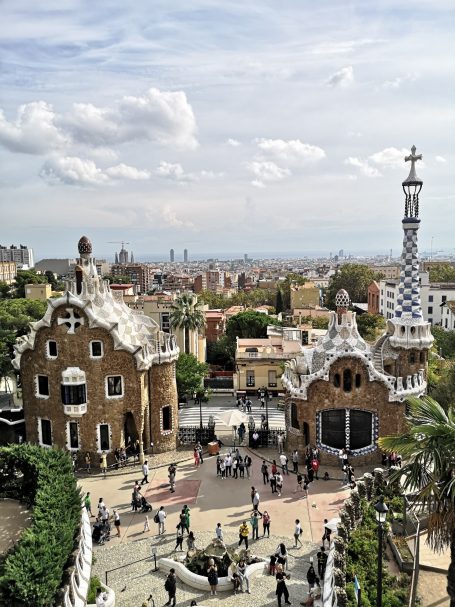 Entrance to Park Güell, featuring unique architecture and city views under a cloudy sky.