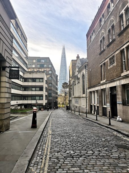 Cobblestone street with buildings lining the sides, featuring The Shard in the distance.