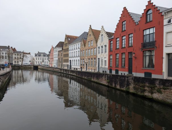 Row of colourful historic buildings along a calm canal under a grey sky.