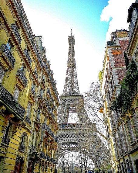 Eiffel Tower rising between historic buildings against a bright blue sky.