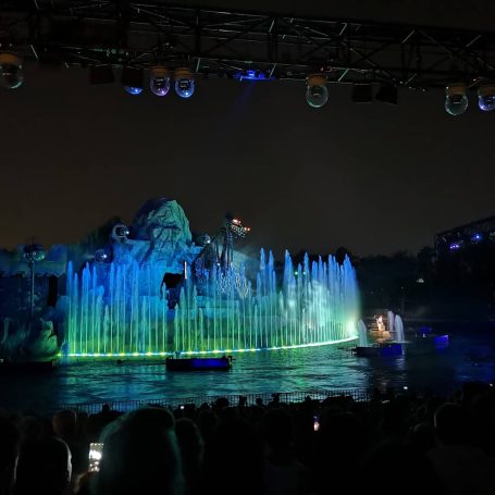 Colourful water fountain display at night with illuminated features and audience in front.