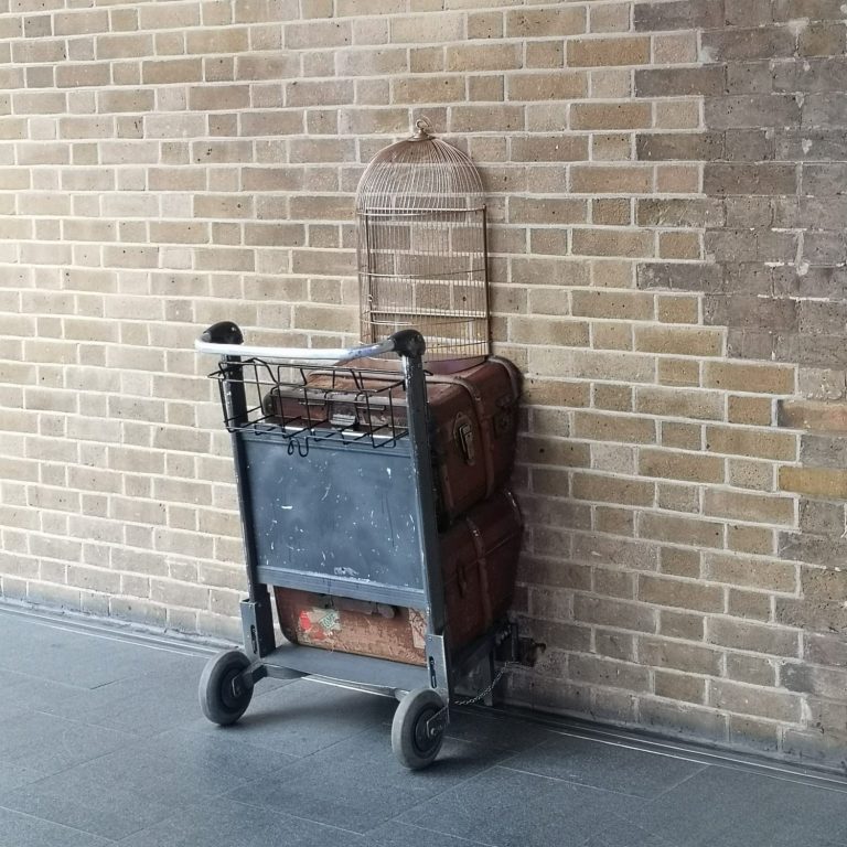 A luggage cart with bags against a brick wall, located at Kings Cross Station in London
