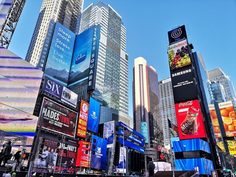 Vibrant Times Square in New York City with tall buildings and lively advertisements against a clear blue sky.