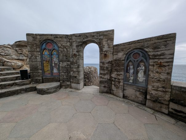 Stone archway with painted wooden doors overlooking the sea on a cloudy day, located at The Minack Theatre