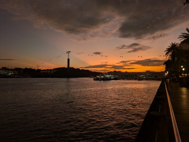 Sunset over a river with a silhouette of a tower and palm trees along the shoreline.