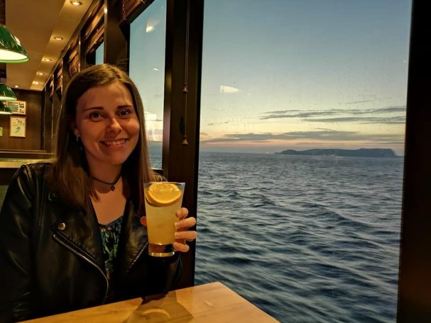 I&B's Founder posing on a cruise ship with a cocktail and the sunset over the ocean in the background.
