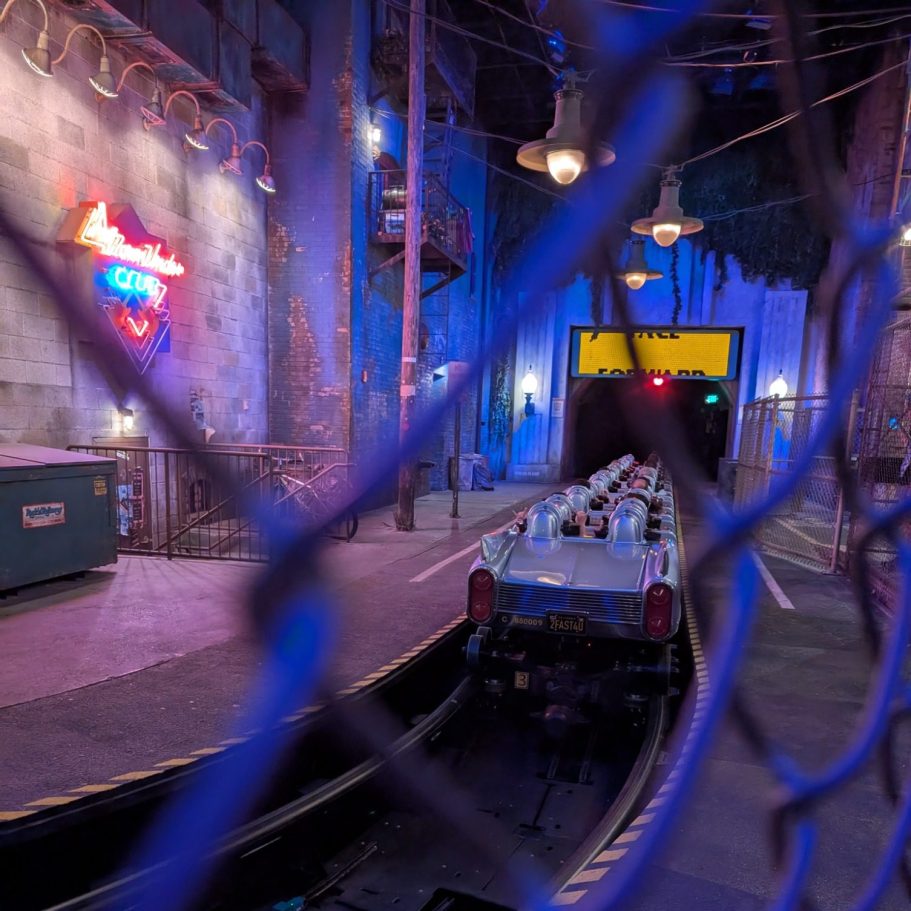 Theme park ride platform with neon lights and a train station entrance. Vintage decor visible.