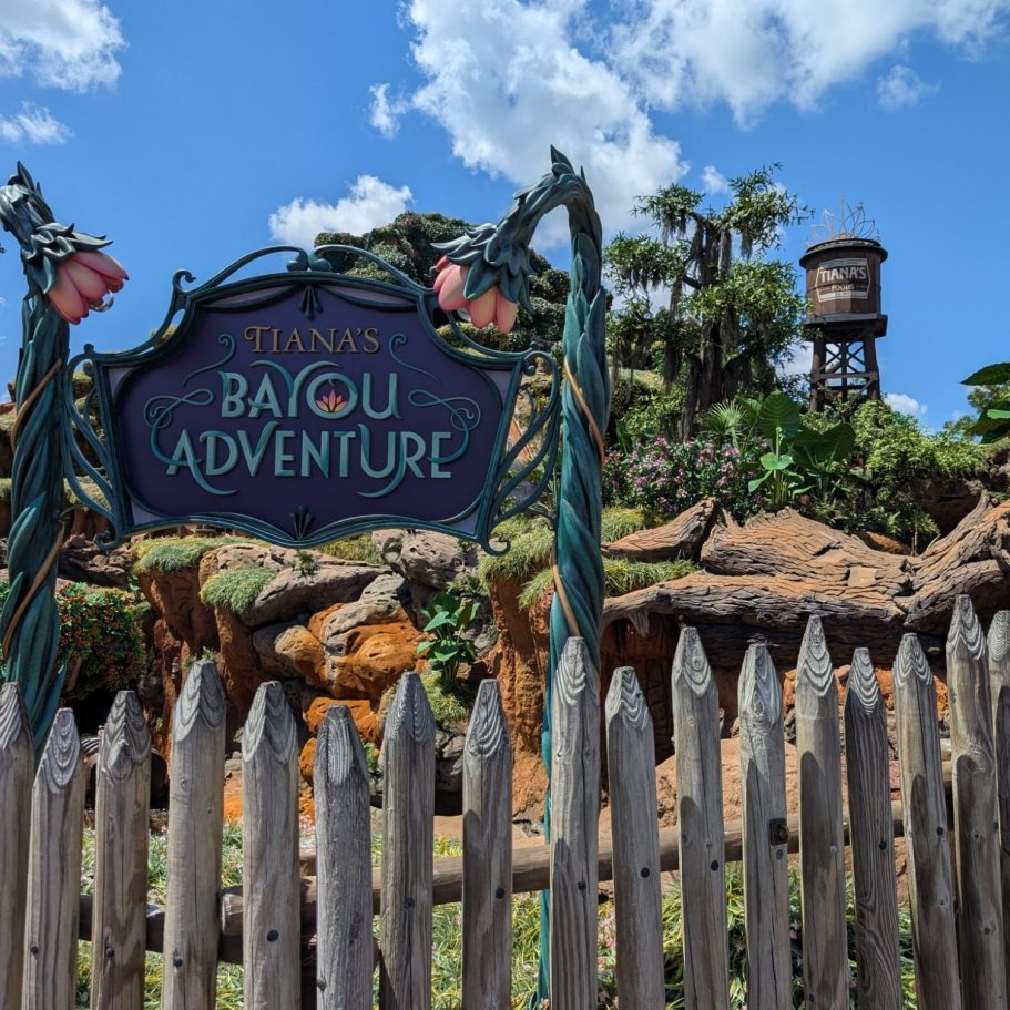 Sign for "Tiana's Bayou Adventure" with a water tower and lush greenery in the background.