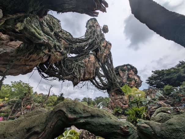 A large, intricately woven tree-like structure surrounded by greenery and cloudy skies.