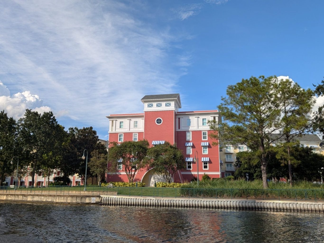 Red and white building beside a calm lake, with trees and blue sky in the background.