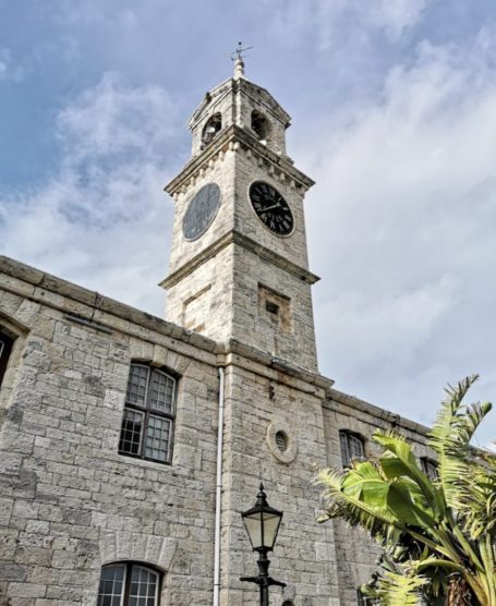 Clock Tower Mall, an historic stone clock tower against a cloudy sky with greenery in the foreground.